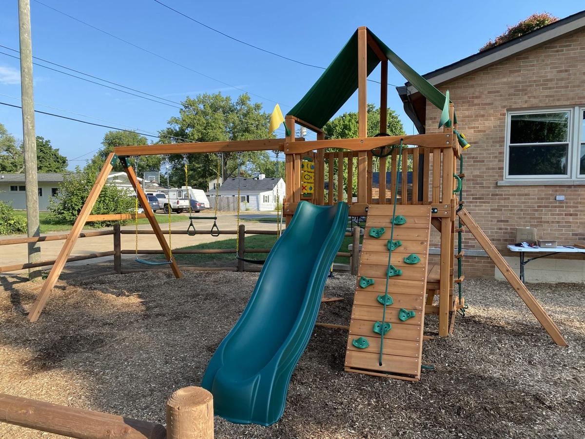 The wooden play set with a green slide, swings and a climbing wall on the masjid grounds